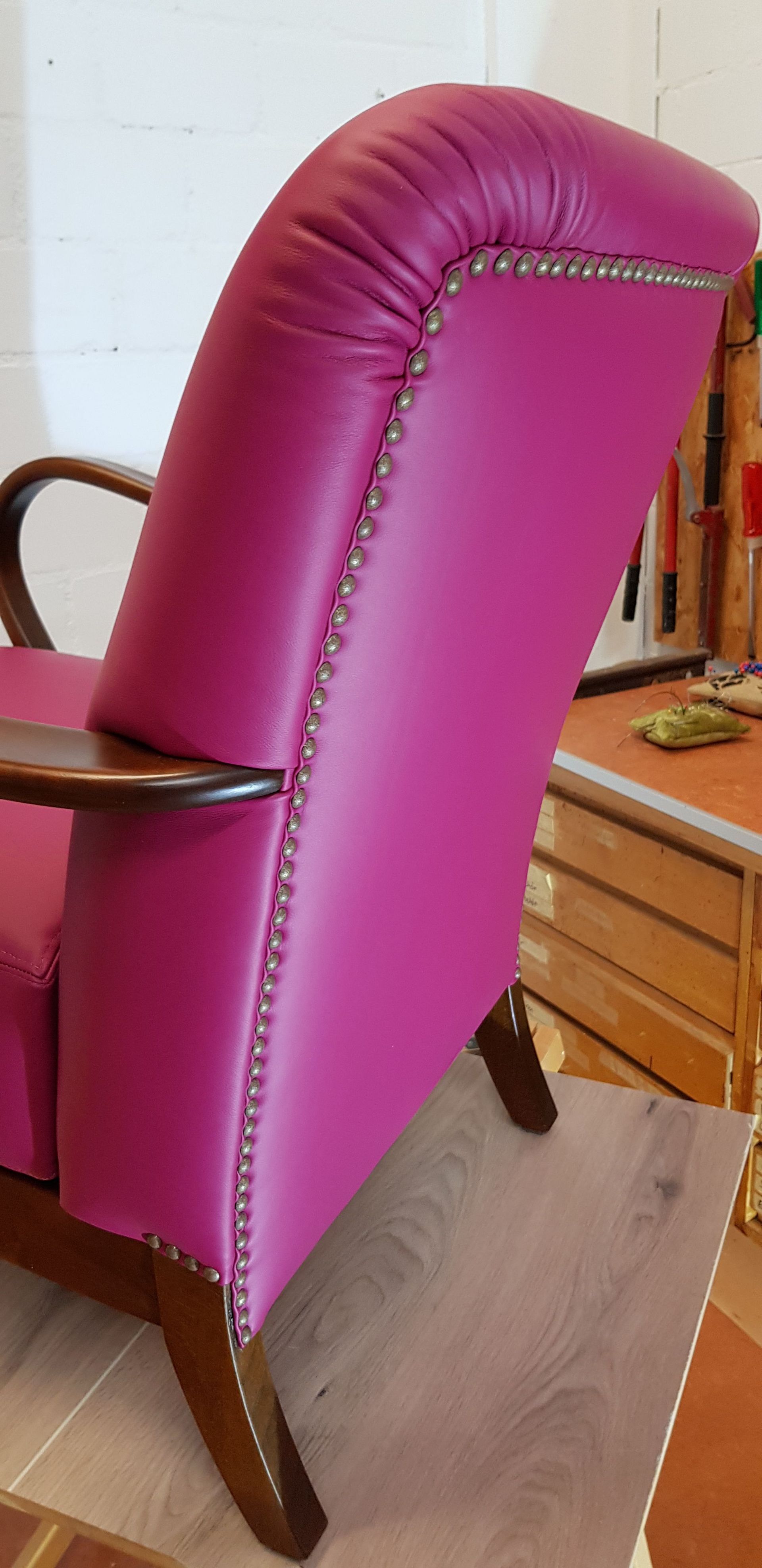 Auf einem Holzboden steht ein rosa Ledersessel mit Holzarmlehnen.