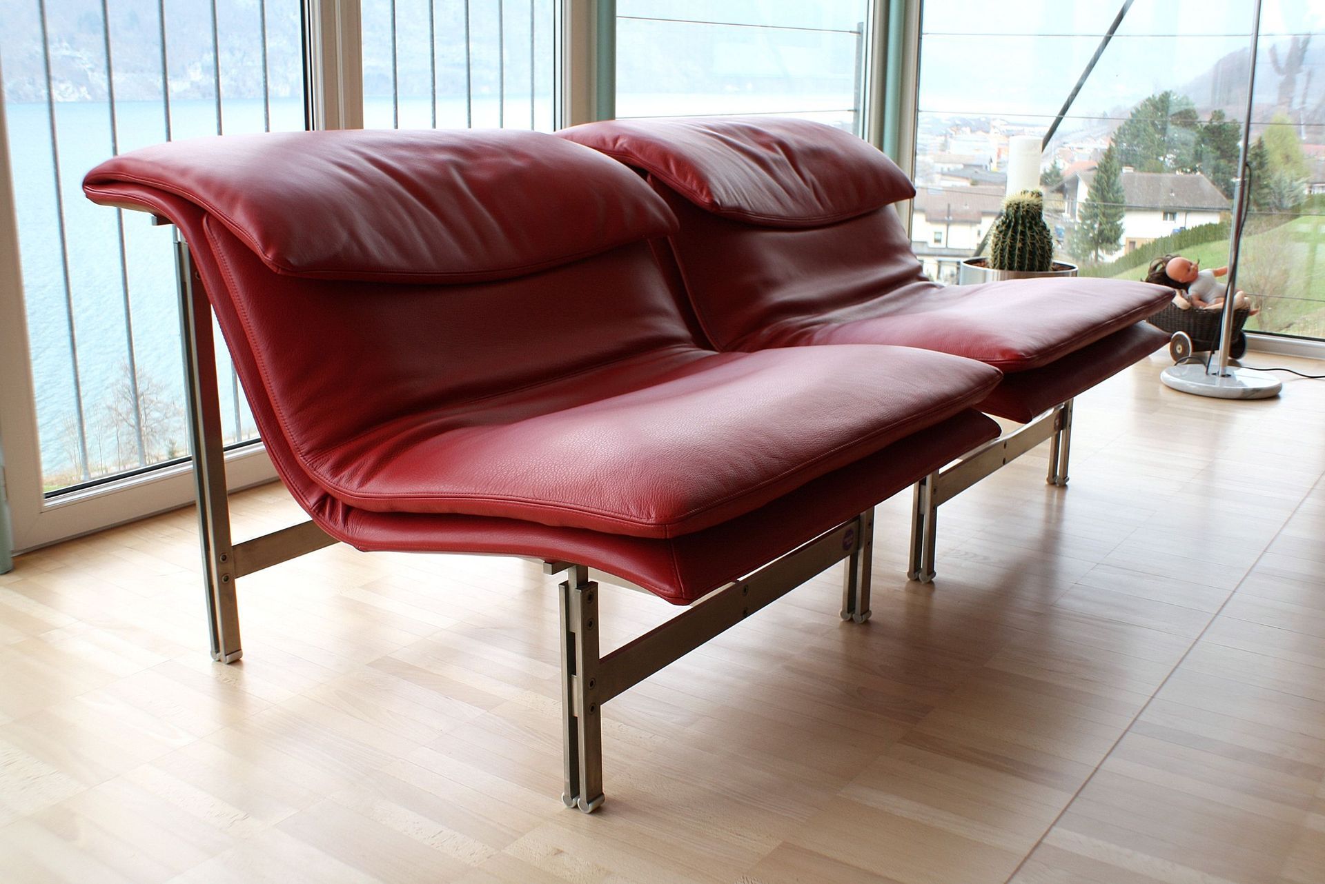 Vor einem Fenster steht auf einem Holzboden ein rotes Ledersofa.