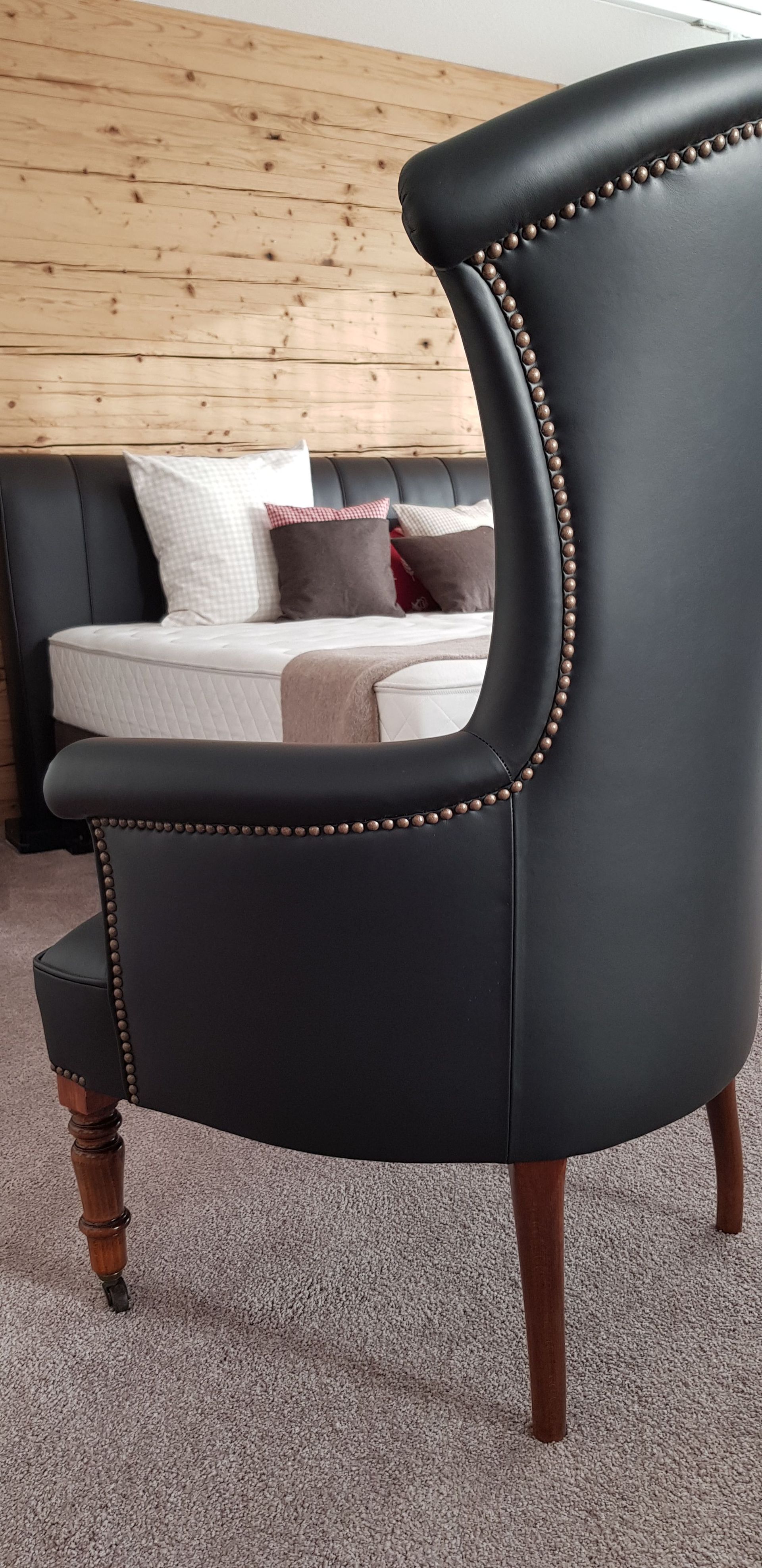 In einem Wohnzimmer steht ein schwarzer Stuhl neben einem Bett.