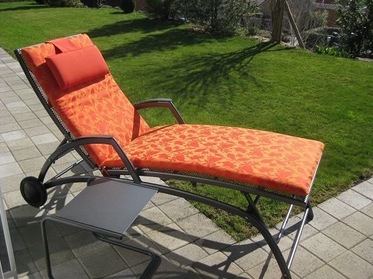 Ein orangefarbener Liegestuhl steht auf einer Terrasse vor einer üppigen grünen Wiese.