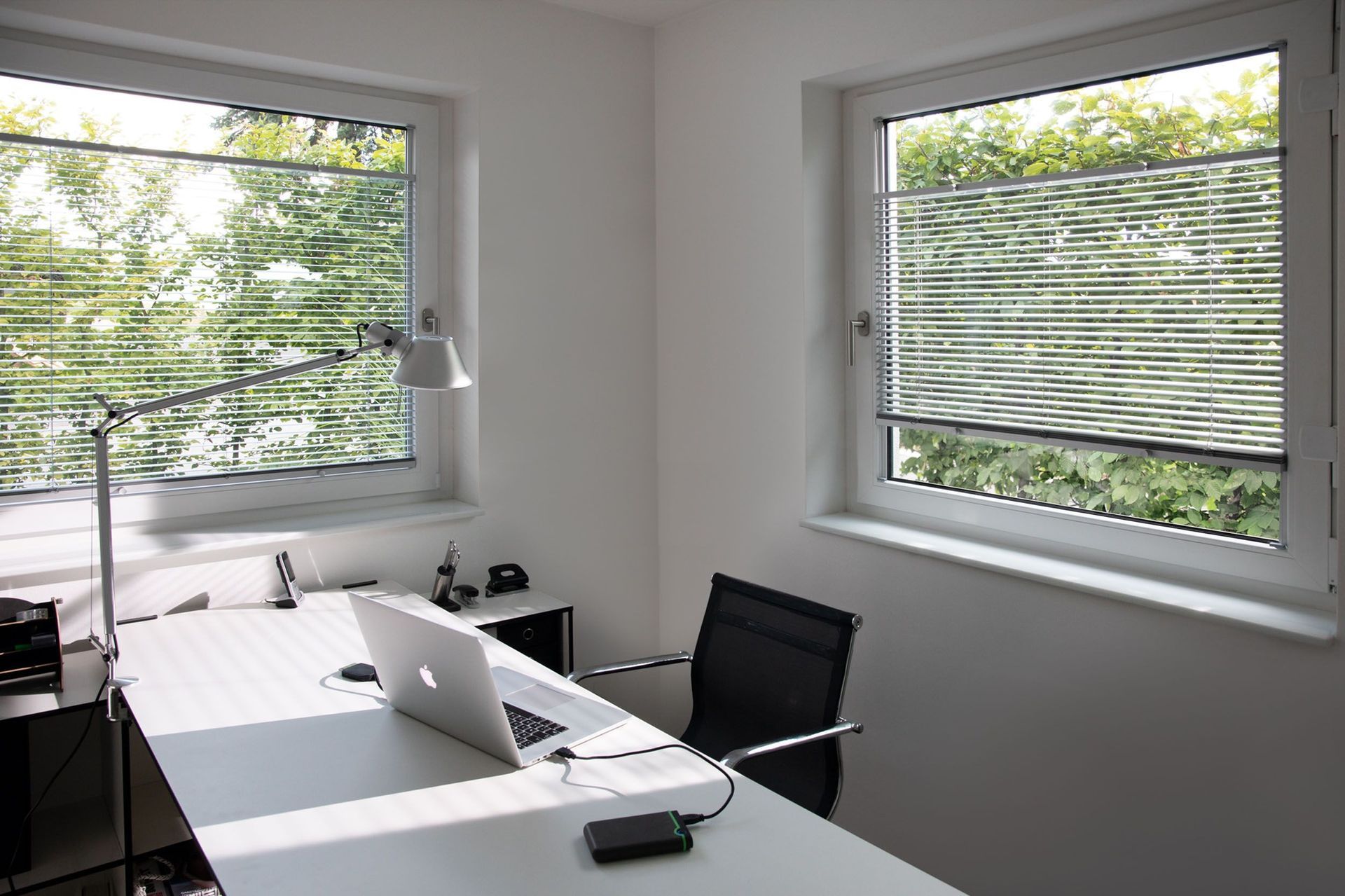 Ein Schreibtisch mit einem Laptop darauf und ein Stuhl vor einem Fenster.