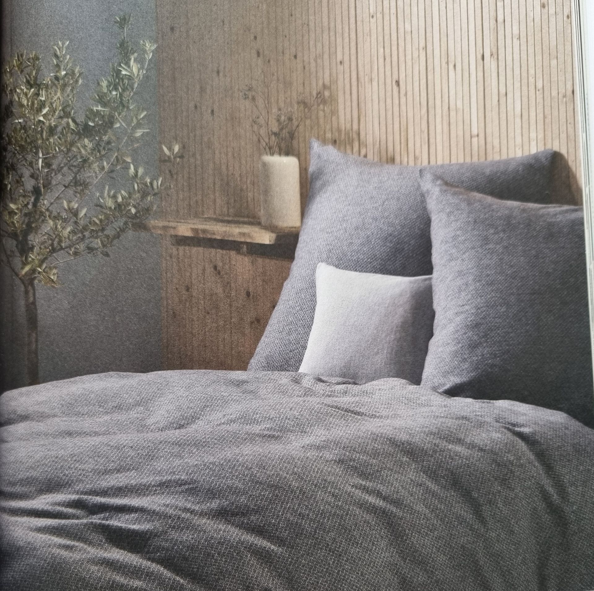 Ein Bett mit einer grauen Bettdecke und Kissen darauf