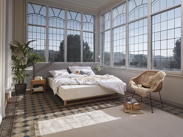 Ein Schlafzimmer mit Bett, Stuhl, Nachttisch und vielen Fenstern.