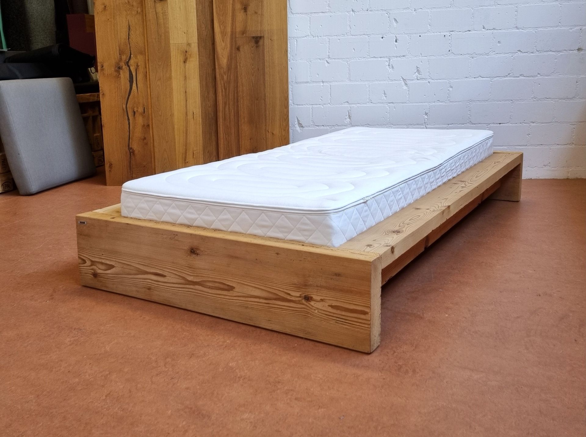 Ein hölzerner Bettrahmen mit einer weißen Matratze darauf.