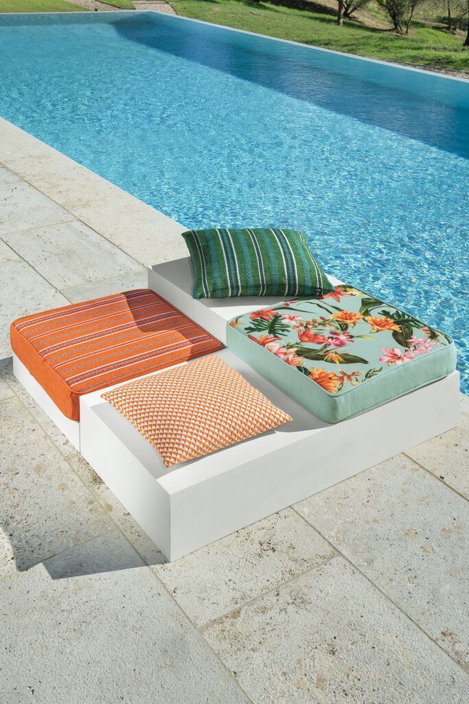 Drei Kissen liegen neben einem Swimmingpool.