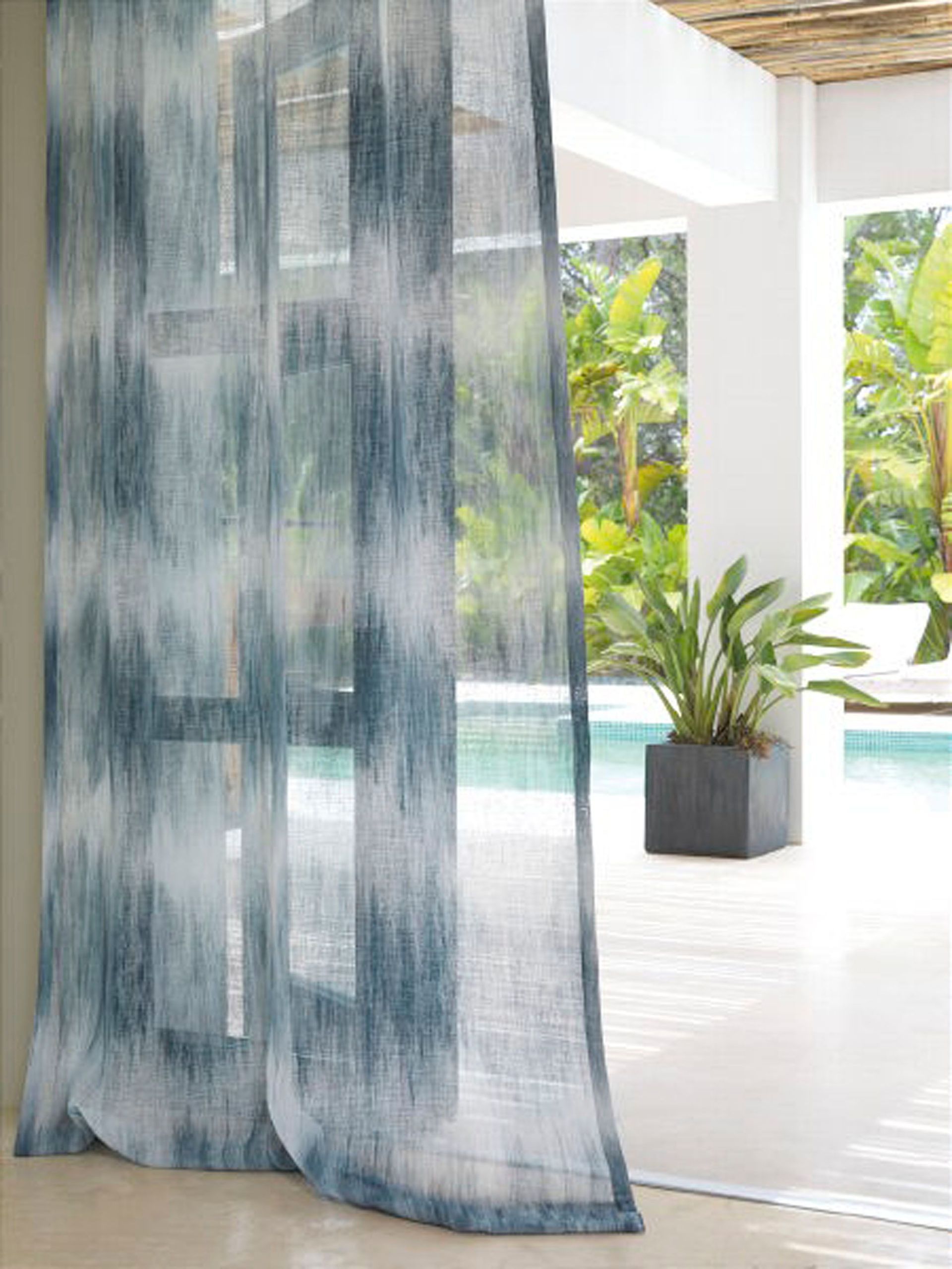 An einem Fenster in einem Zimmer hängt ein blau-weißer Vorhang.