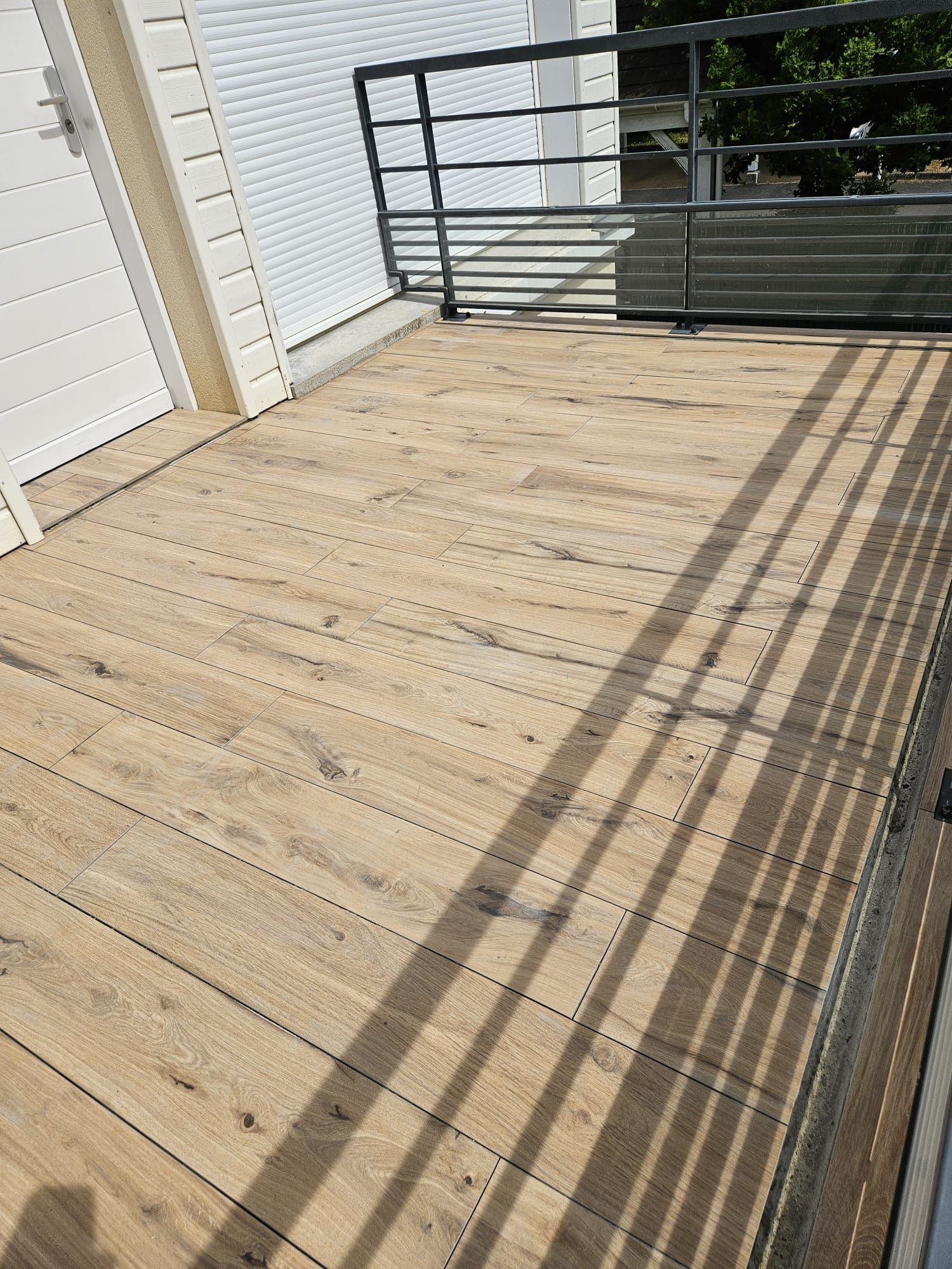 Balcon avec carrelage effet bois avec rambarde en métal et ombres rayées dues au soleil