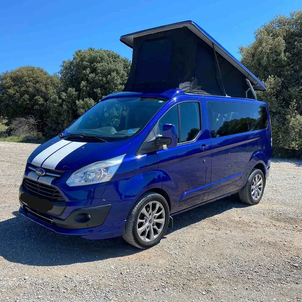 Una camioneta azul con techo negro está estacionada en un estacionamiento de grava.
