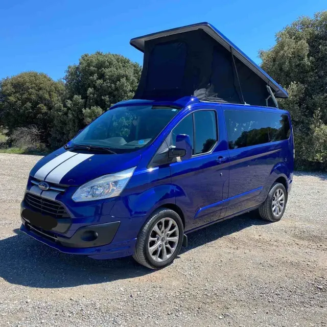 Una camioneta azul con techo negro está estacionada en un estacionamiento de grava.