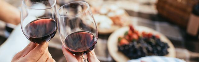 Ein Glas Rotwein, Flaschen und ein Korkenzieher auf einer rustikalen Holzoberfläche.