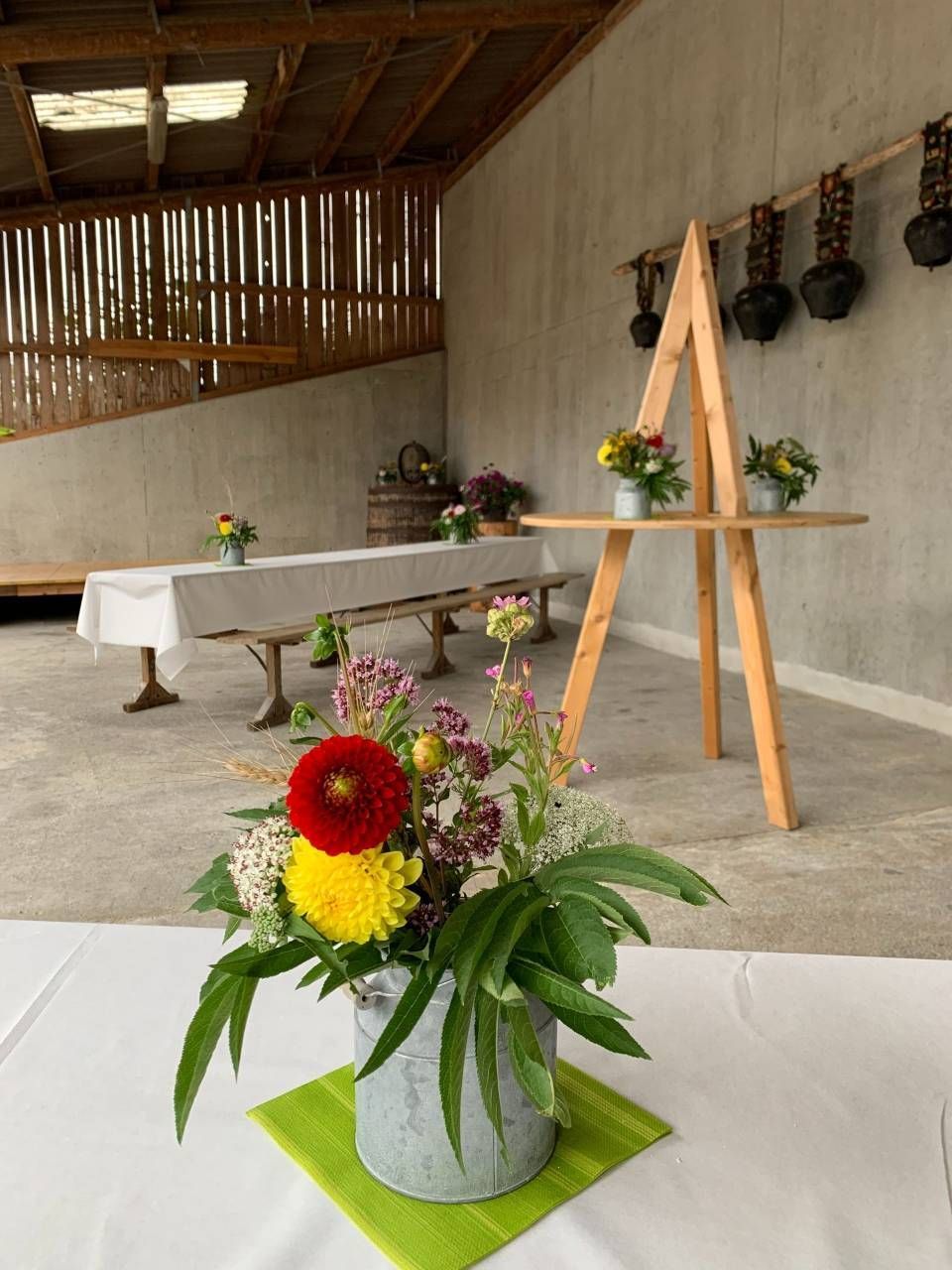 Eine mit Blumenarrangements gedeckte Tafel in einer rustikalen Scheune.