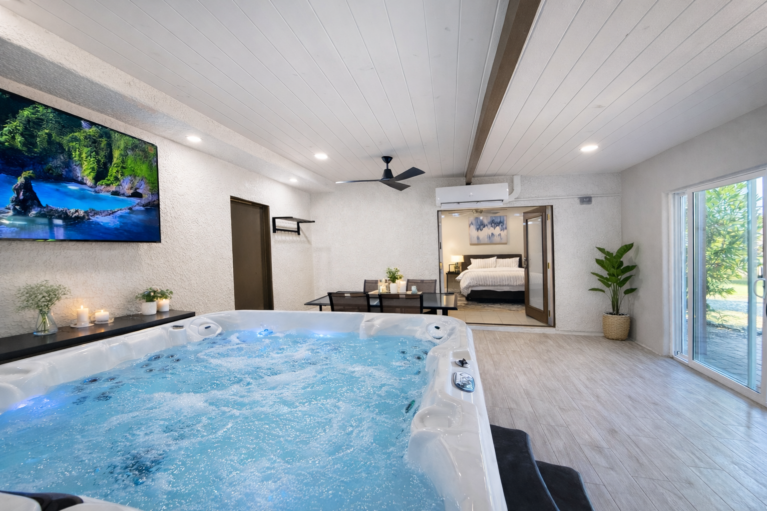 Indoor jacuzzi with bubbles, a TV displaying a scenic view, and a view into a bedroom with a bed.