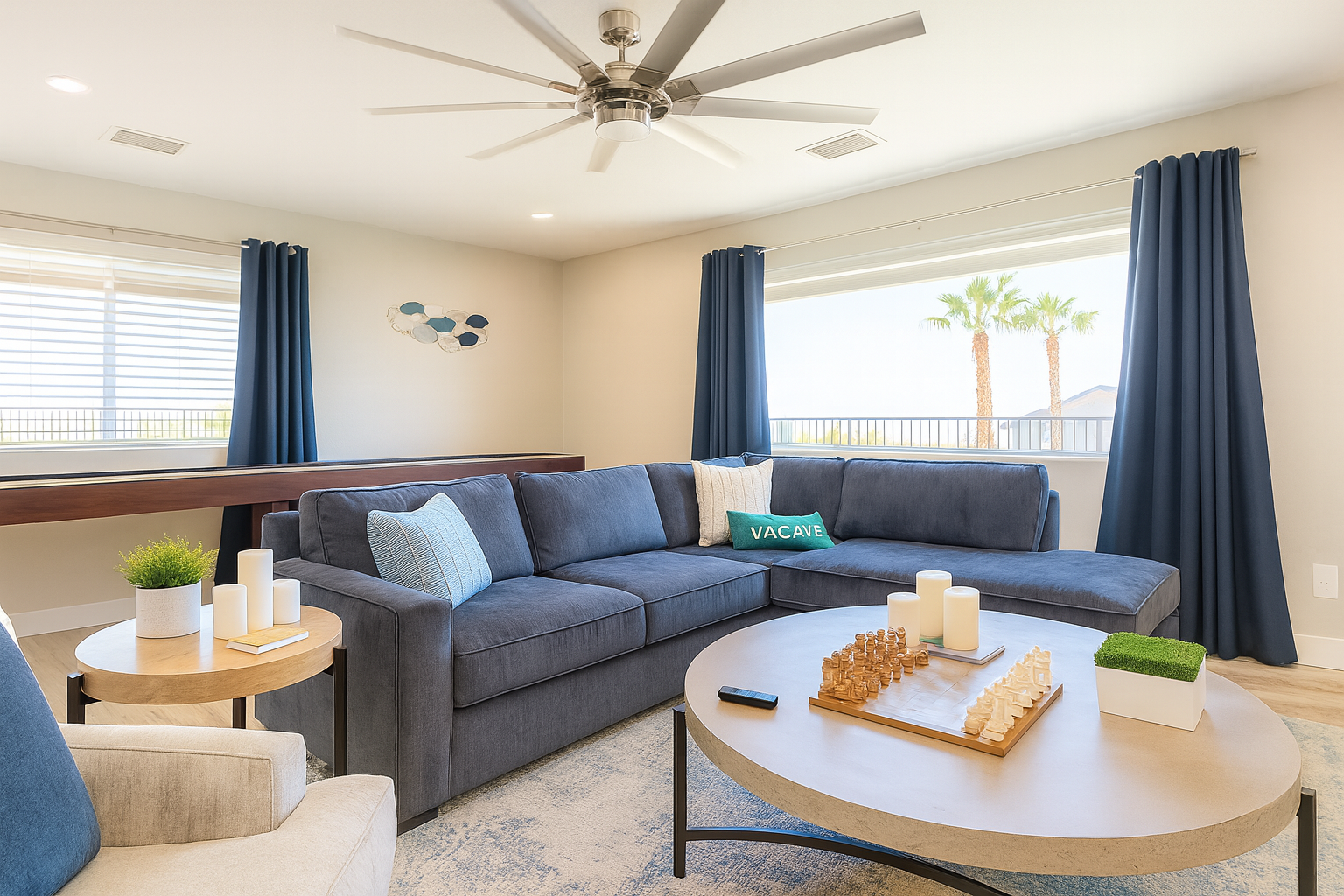 Living room with navy blue sectional, round coffee table, and large window with palm trees outside.