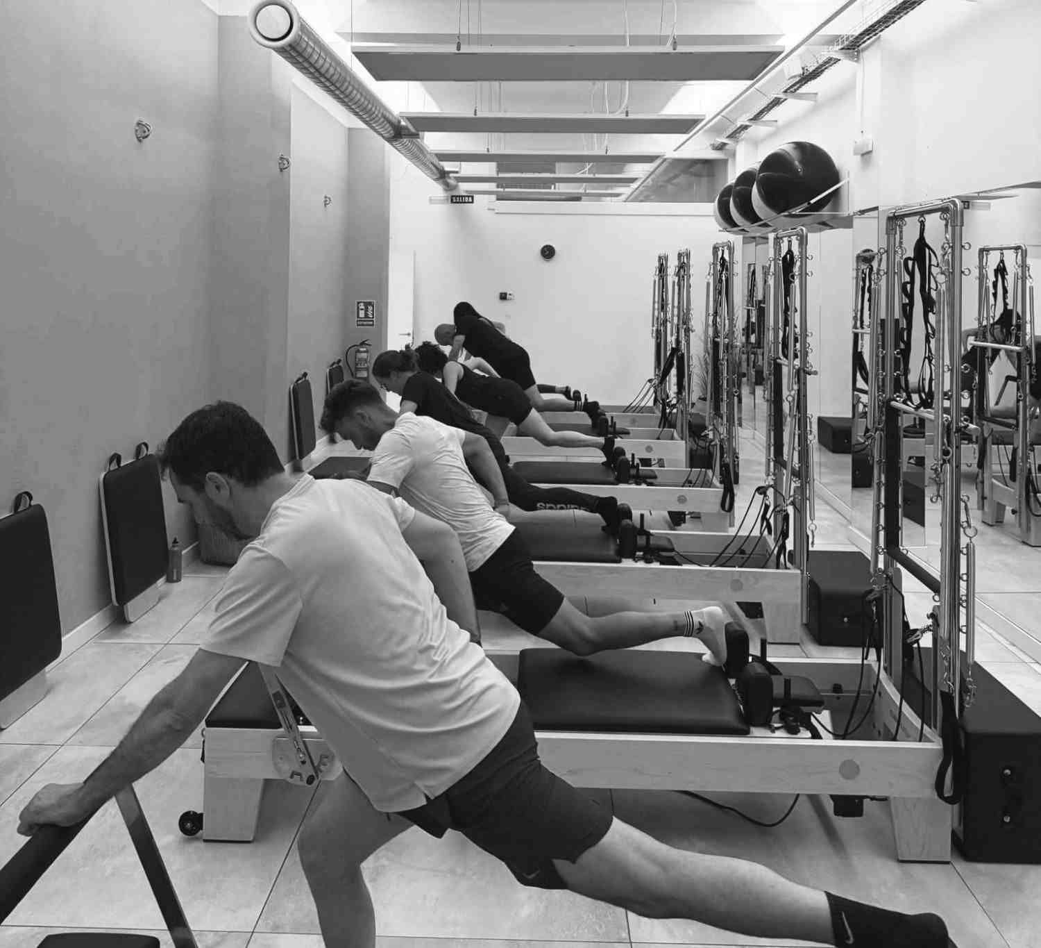 Estudio de pilates con máquinas reformer, espejos y pelotas de ejercicio bajo una iluminación intensa en el techo