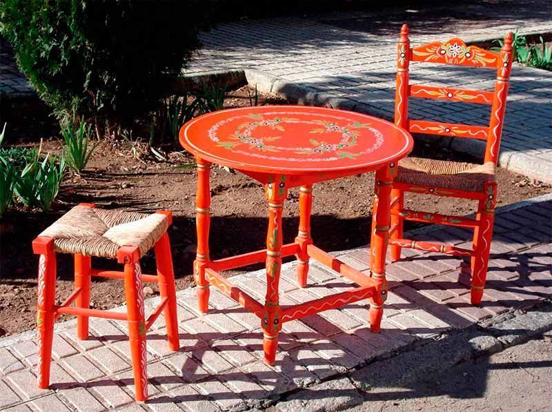 Una mesa roja con dos sillas y un taburete en una acera de ladrillos.