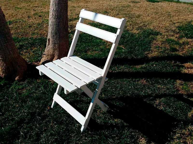 Una silla plegable blanca está sentada en el césped al lado de un árbol.