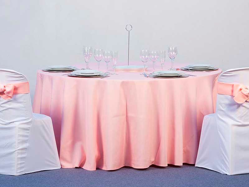 Una mesa con un mantel rosa y sillas blancas.