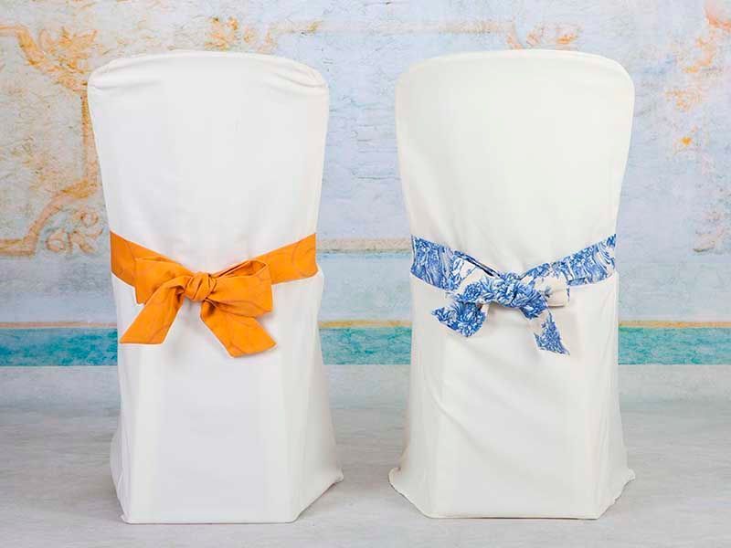 Dos fundas de silla blancas con lazos naranjas y azules están sobre una mesa.