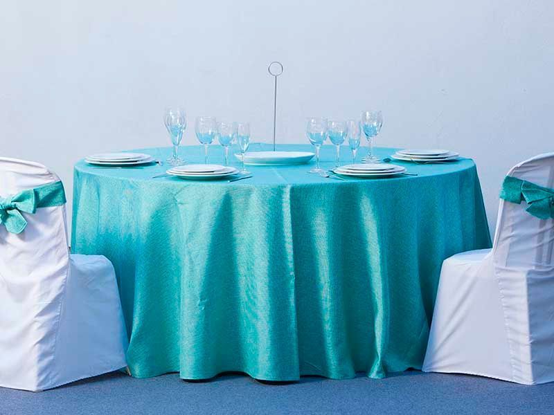 Una mesa con un mantel turquesa y sillas blancas.