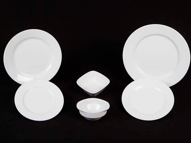 Un conjunto de platos y cuencos blancos sobre un fondo negro.