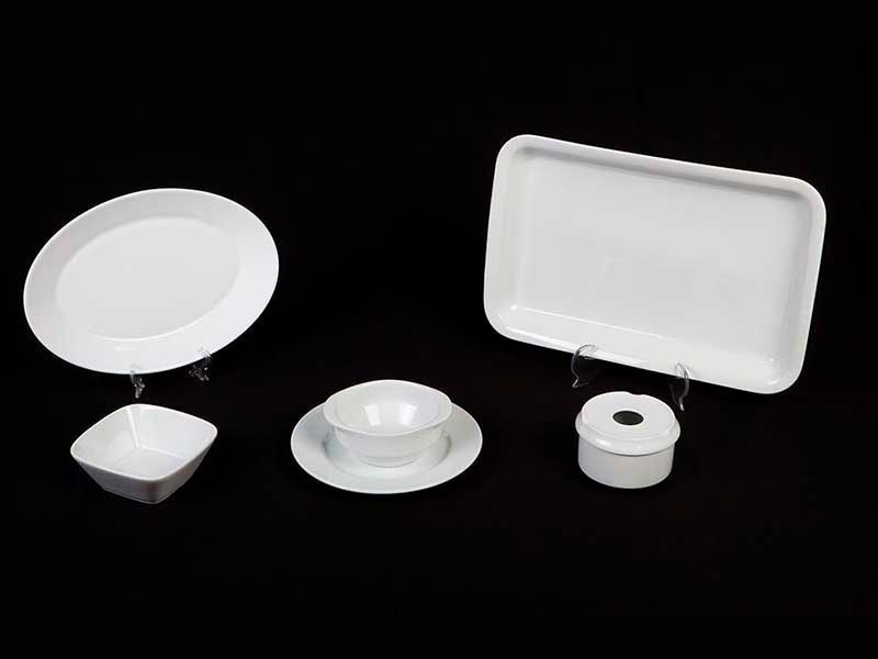 Un grupo de platos, cuencos y bandejas blancos sobre un fondo negro.