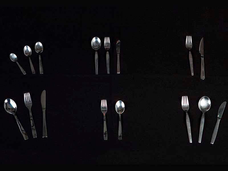Una fila de cubiertos que incluye tenedores, cucharas y cuchillos sobre un fondo negro