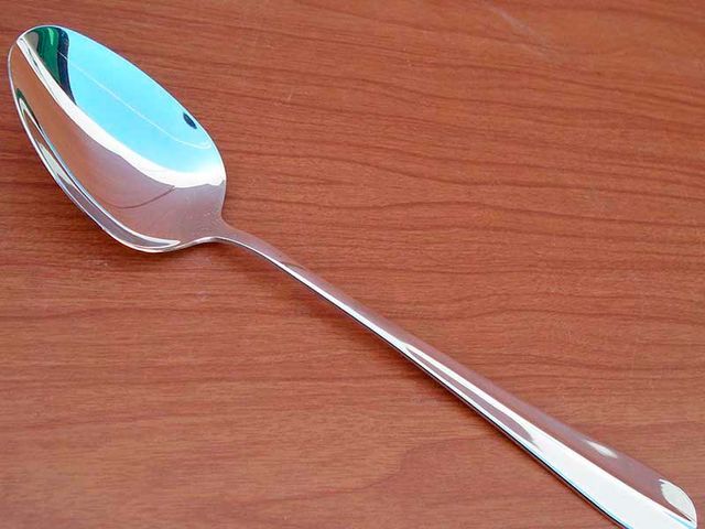 Una cuchara de plata está sobre una mesa de madera.