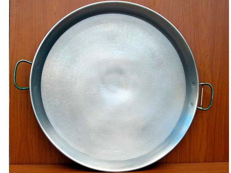 Una gran sartén de aluminio con asas está sobre una mesa de madera.