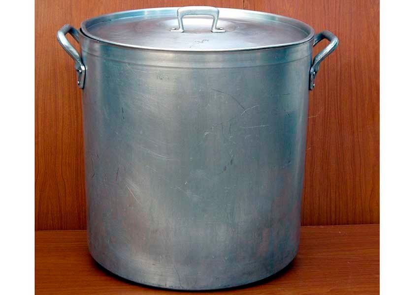 Una olla grande de aluminio con tapa está sobre una mesa de madera.