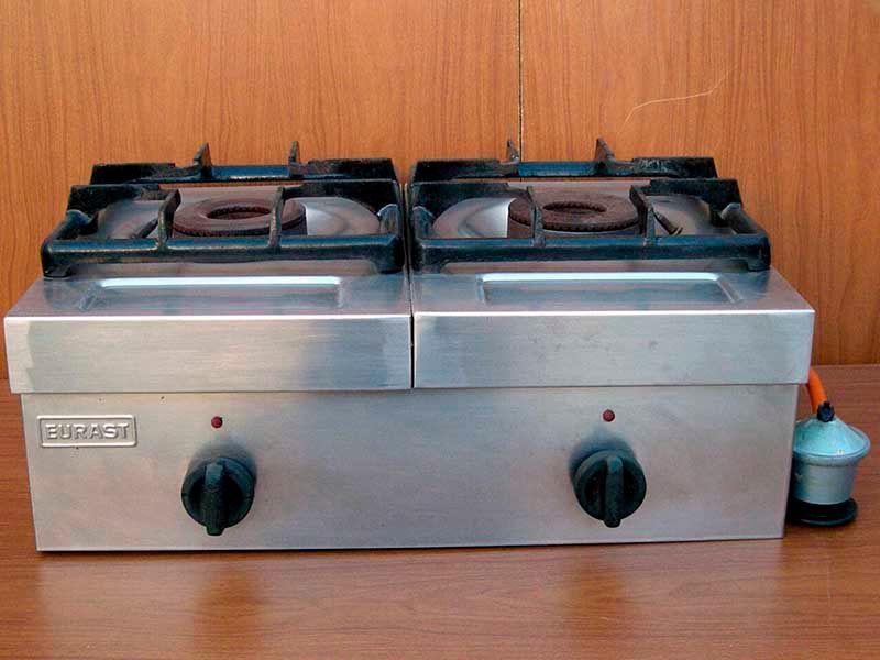 Una estufa de gas de acero inoxidable con dos quemadores está sobre una mesa de madera.