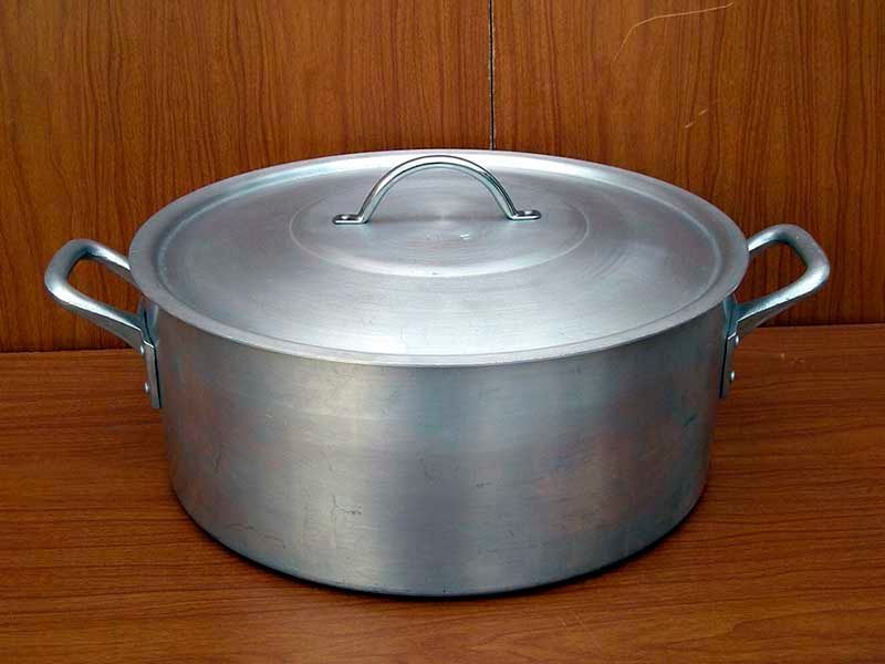 Una olla de aluminio con tapa está sobre una mesa de madera.