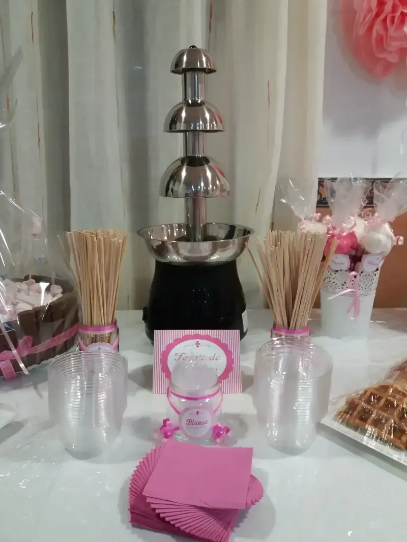 Una mesa con una fuente de chocolate, pajitas, vasos y servilletas encima.