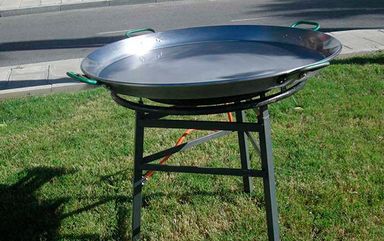 Una sartén grande reposa sobre un soporte de metal en el césped.