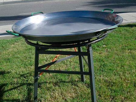 Una sartén grande reposa sobre un soporte de metal en el césped.