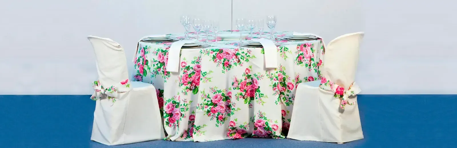 Una mesa con un mantel floral y sillas blancas sobre una mesa azul.
