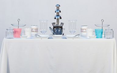 Una mesa con un mantel blanco y una fuente de chocolate encima.