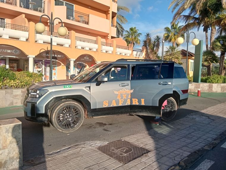 Un SUV plateado todoterreno estacionado junto a un edificio de un complejo turístico con palmeras y farolas.