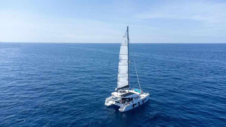 Catamarán navegando sobre un océano azul en calma bajo un cielo despejado, visto desde arriba.