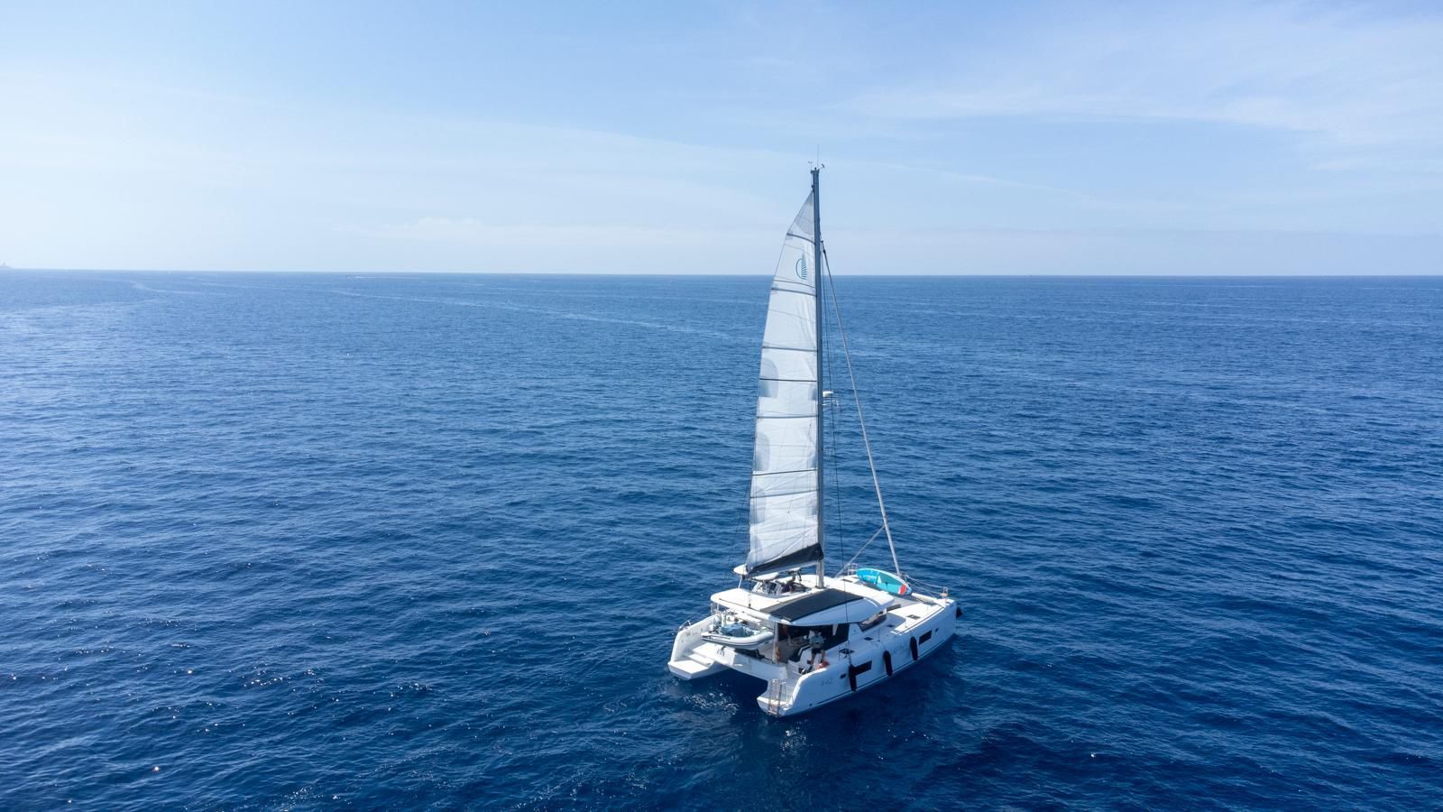 Catamarán navegando en un océano azul tranquilo bajo un cielo despejado.