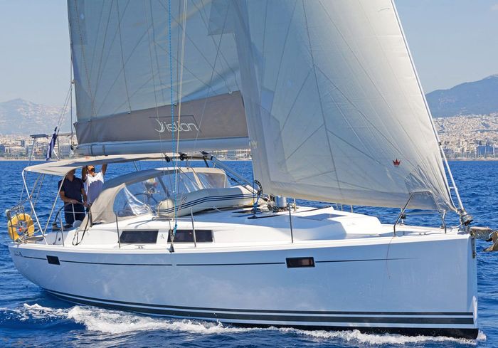 Velero blanco navegando sobre aguas azules con las velas izadas, con el perfil del puerto al fondo.