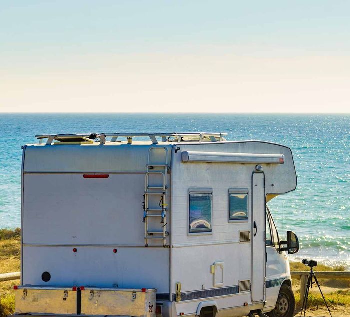 Una autocaravana blanca aparcada junto al mar bajo un cielo despejado, con las olas del océano al fondo.
