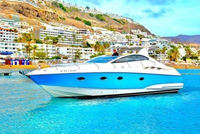 Yate a motor azul y blanco sobre agua turquesa, con edificios y una colina al fondo.