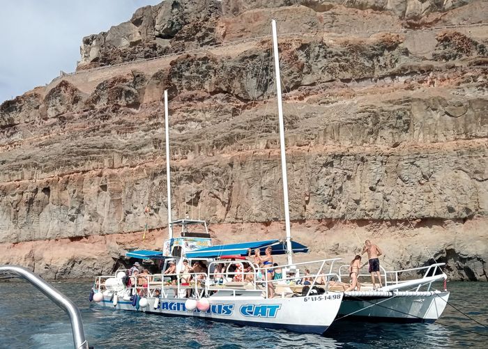 Barco turístico con pasajeros en aguas azules junto a un acantilado rocoso del desierto.