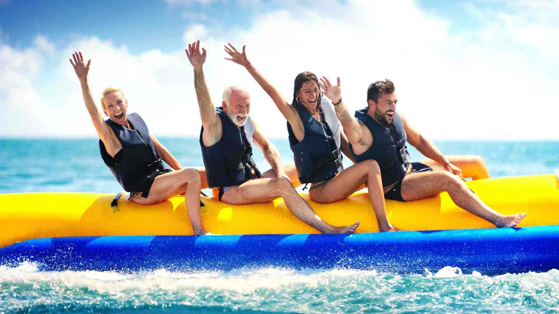 Cuatro personas en un barco banana en el océano con los brazos levantados, sonriendo.