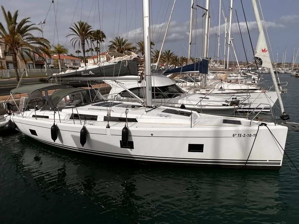 Velero blanco atracado en un puerto deportivo, palmeras al fondo.
