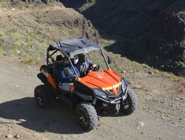 Persona conduciendo un buggy todoterreno naranja en un sendero rocoso de montaña.