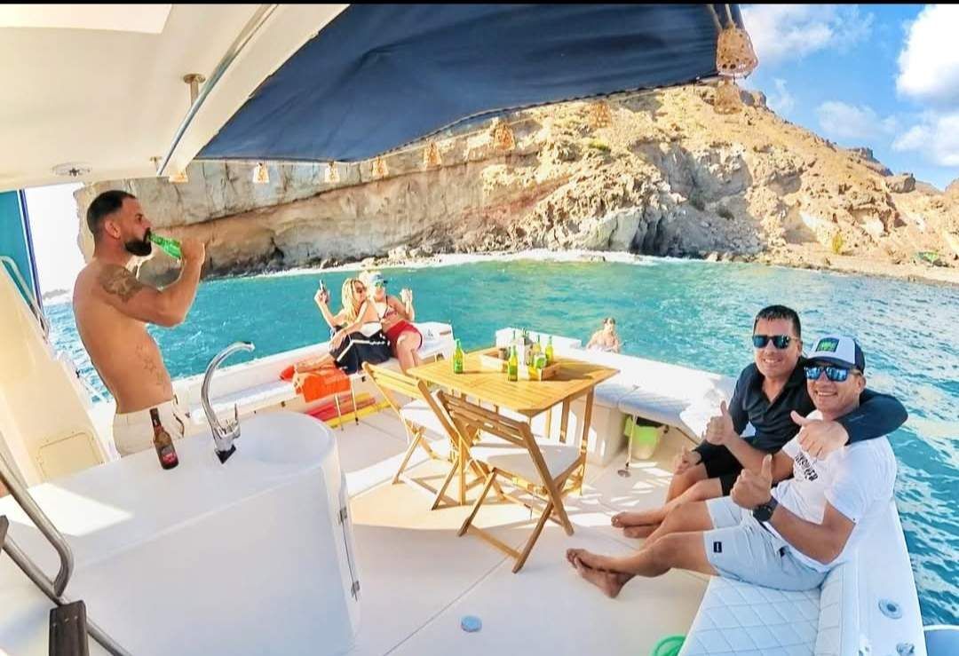 Gente en un barco cerca de una costa rocosa, bebiendo y disfrutando.