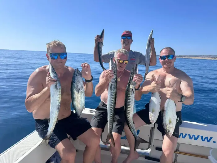 Tres personas en un bote sosteniendo peces grandes, con un océano azul en calma de fondo.