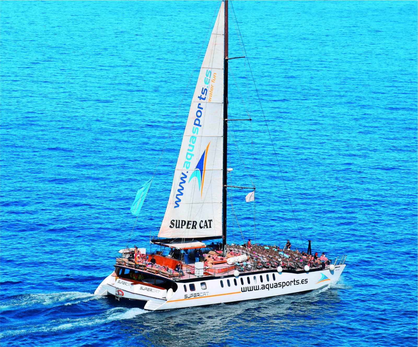 Velero blanco con una vela alta navegando sobre aguas azul brillante del océano.