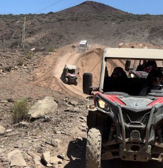 Buggies todoterreno circulando por un sendero rocoso en el desierto con una montaña al fondo.
